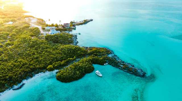 Turquoise water and a pale sandbar curve around a green island, with a few small boats nearby.
