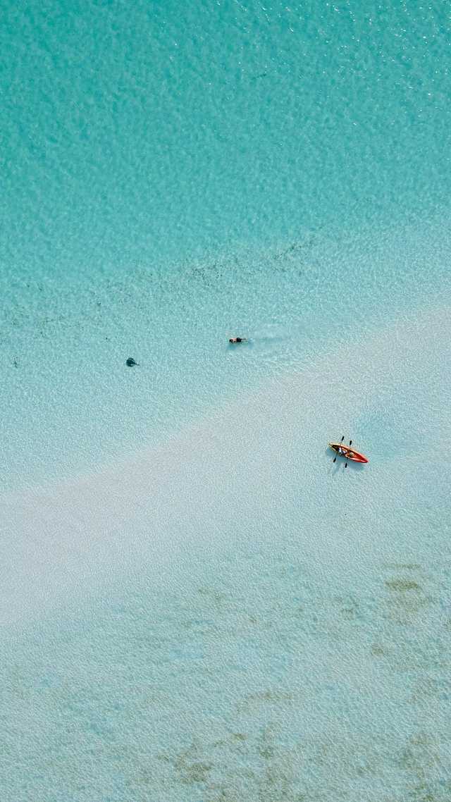Two people stand in clear shallow water beside a small boat.
